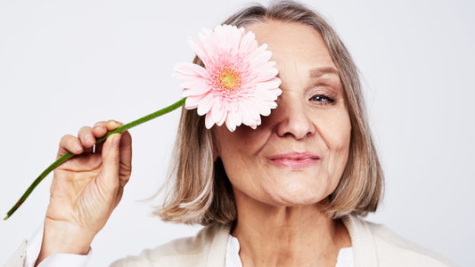 Mujer madura sosteniendo una flor rosa frente a su rostro